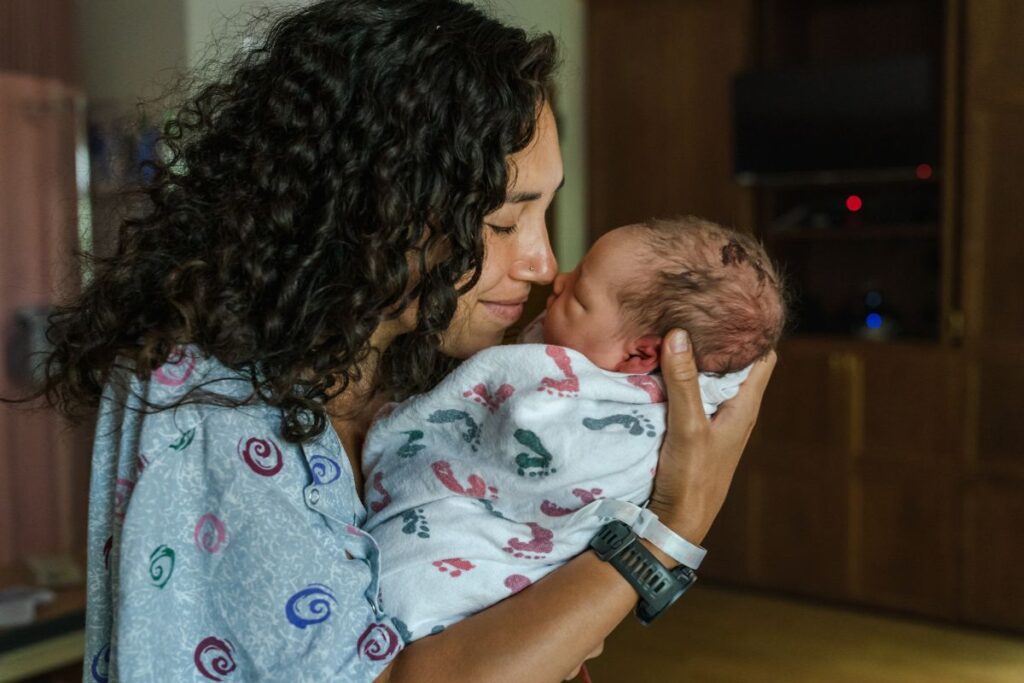 Mother with curly black hair holding a newborn baby face-to-face.